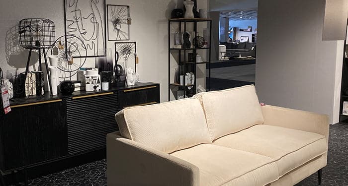 Ein weißes Sofa, im Hintergrund ein schwarzes Sideboard mit abstrakten Kunstwerken darauf
