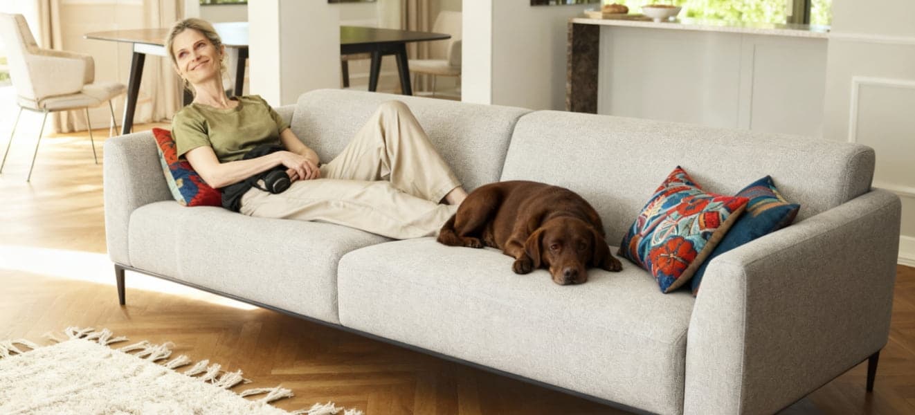Eine Frau liegt mit einem braunen Hund auf einem grauen Sofa.