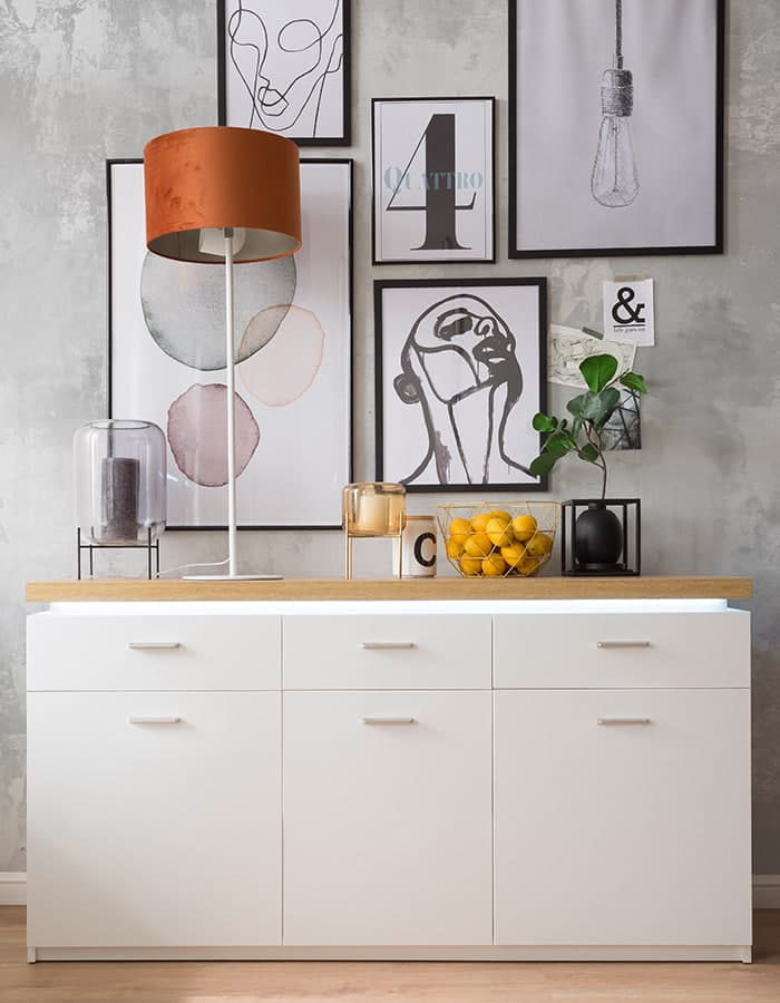 Weiße Kommode vor einer Wand mit vielen bunten Bildern