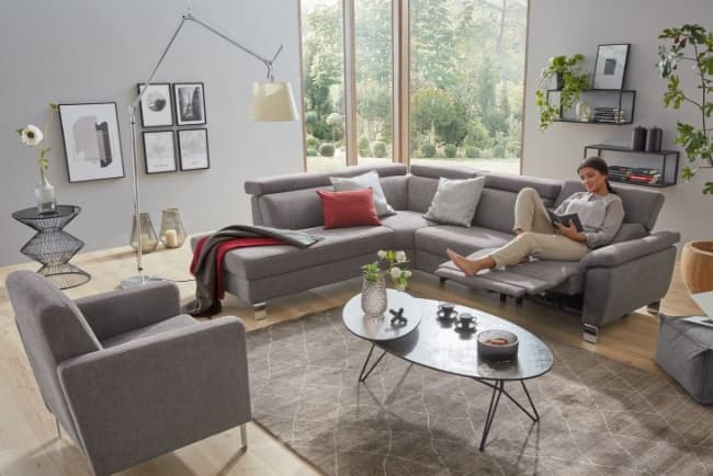 Ein modernes Wohnzimmer mit grauem Sofa und grauem Sessel. In der Mitte ein schwarzer Couchtisch