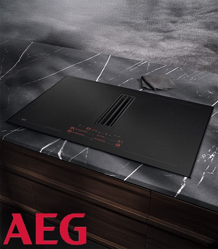 Ein schwarzes AEG-Induktionskochfeld auf einer dunklen Marmor-Arbeitsplatte. Unten links befindet sich ein rotes AEG-Logo.