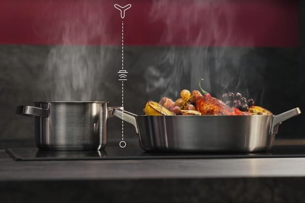 Edelstahlkochfeld mit zwei Töpfen und integriertem Dunstabzug, der den aufsteigenden Kochdampf zwischen den Töpfen nach unten absaugt.