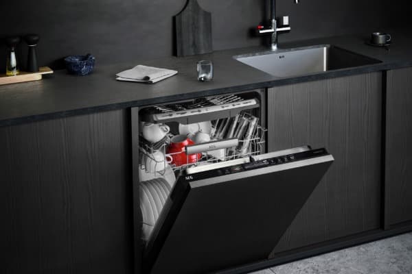 Geöffnete Einbau-Spülmaschine mit Geschirr und roten Tassen in einer modernen Küche mit dunklen Fronten.