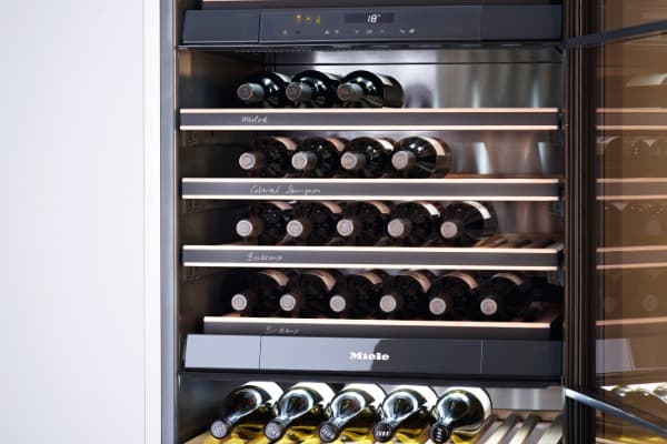 Geöffneter Miele-Weinkühlschrank mit mehreren beleuchteten Regalböden und übersichtlich gelagerten Weinflaschen bei 18 °C.